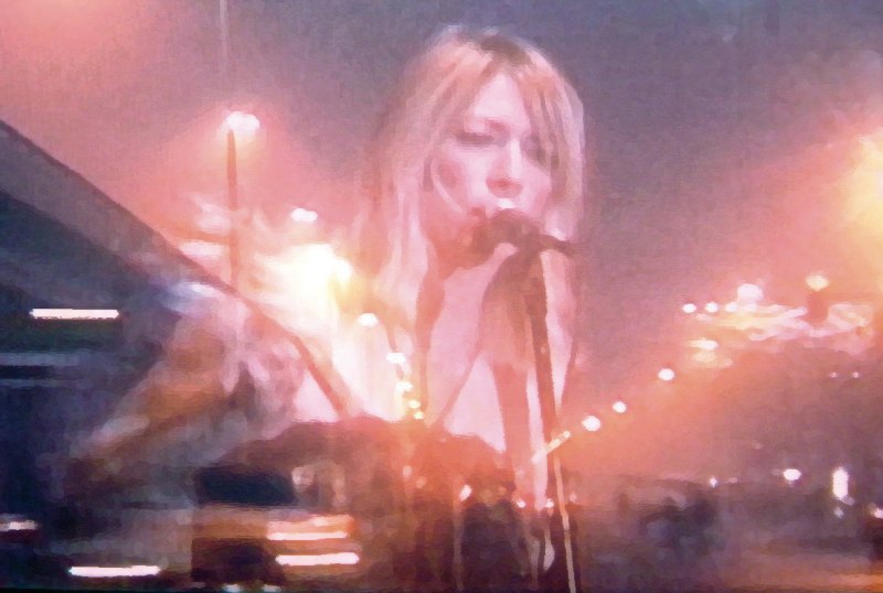 Image shows singer Kim Gordon performing, overlayed is the image of a motorway at night.