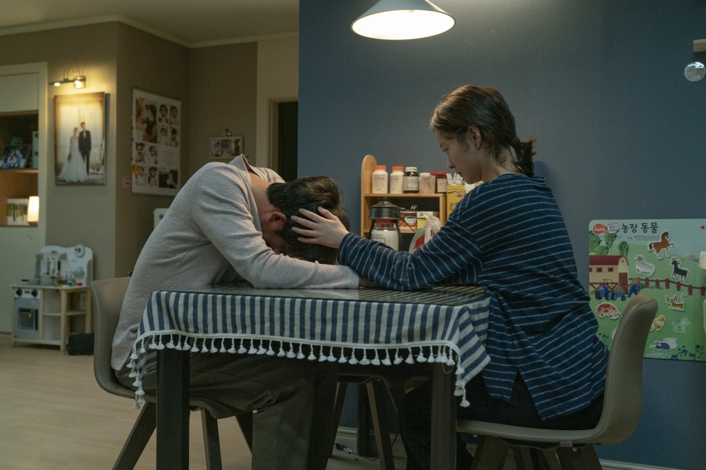 Dae.hyun (Gong Yoo) is sitting at the dinner table with his head lowered while sobbing. Ji-young (Jung Yumi) is sitting opposite to him and caressing his head.