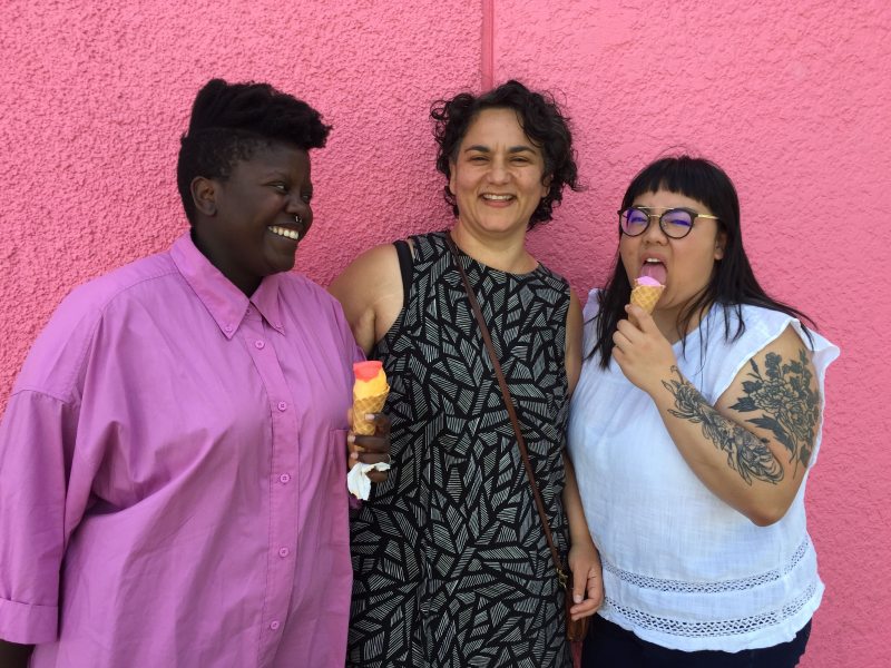 Well Rounded director Shana Myara with cast members Lydia and Joanne in front of a bright pink wall, eating ice cream