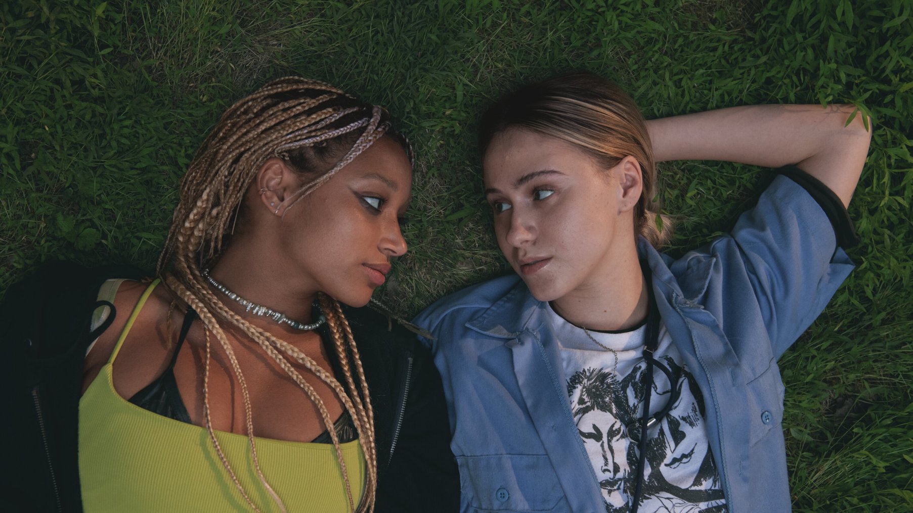 A still from 'Bodies Bodies Bodies'. Sophie (Amandla Stenberg) and Bee (Maria Bakalova) share a moment looking at each other laying on the grass.