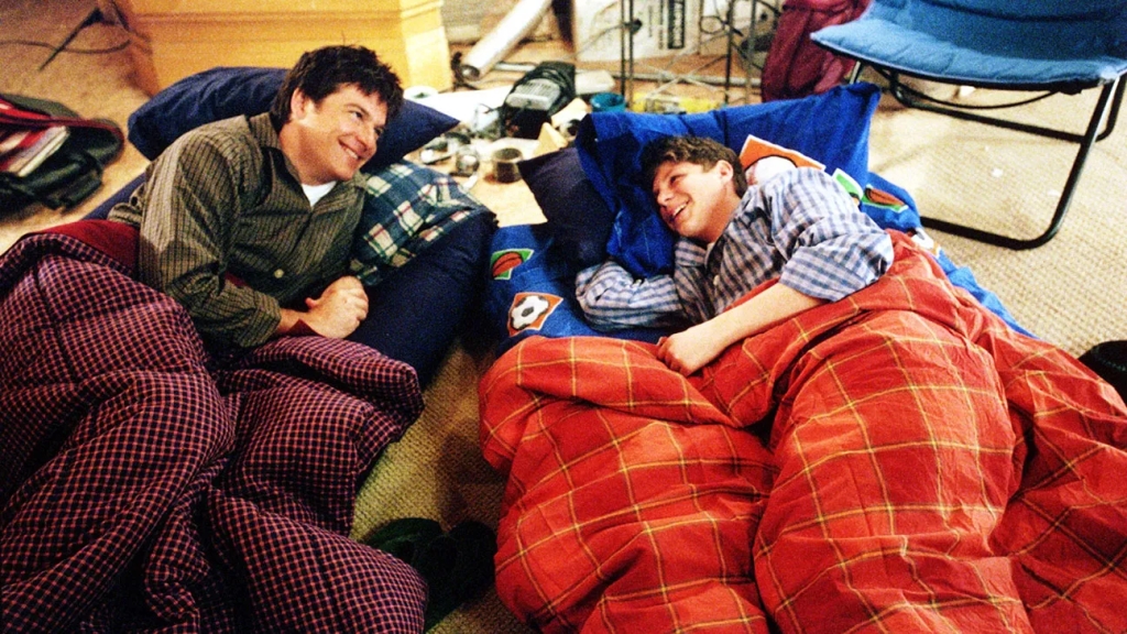 Still showing Michael and George Michael from the pilot episode in their respective beds (mattresses on the floor) as they are smiling and laughing.