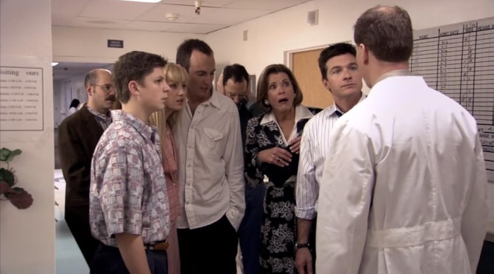 George Michael, Tobias, Lindsay, Gob, Buster, Lucille and Michael shown standing in a hospital corridor in front of a doctor (whose back is only shown in the frame). They look distressed and worried. 