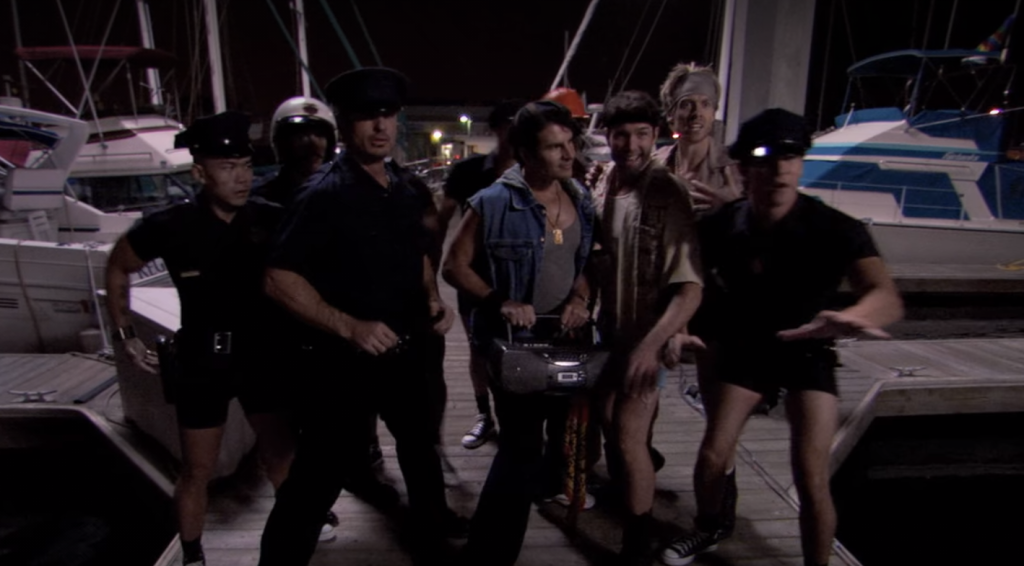 Gob's group of stripper friends seen preparing for the drug bust happening at the pier near the family yacht. They are all posing, wearing outfits typical of strippers, including police uniforms (with short shorts). One of the guys is seen holding a boom box. 