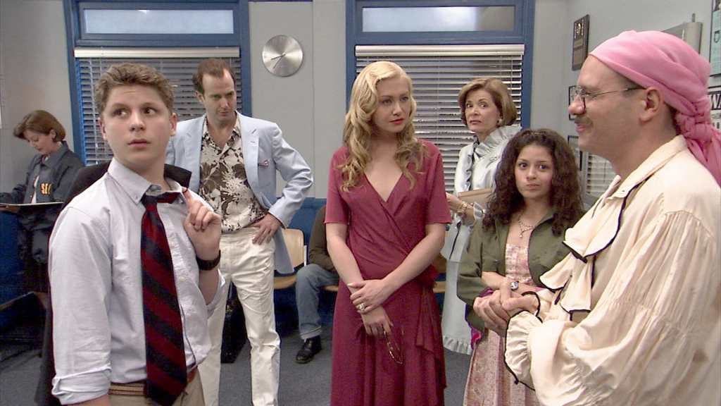 (From left to right) George Michael, Gob, Lindsay, Lucille, Maeby, and Tobias stand in the middle of a police station looking in different directions. Most noticeably, Lucille looks with disgust towards Tobias, who is wearing a pirate-inspired blouse and a pink head scarf. 