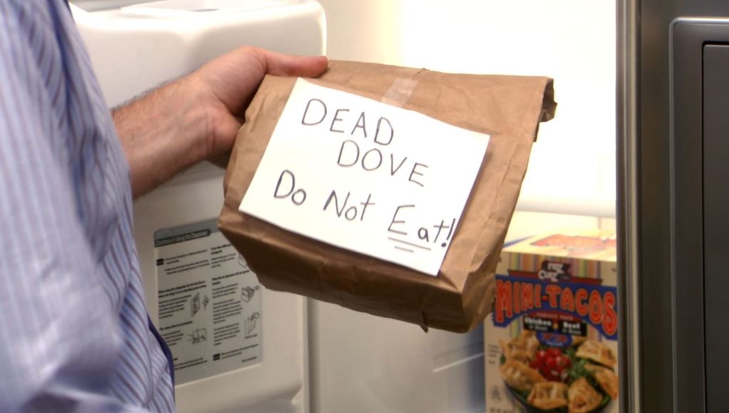 Close up showing the inside of a refrigerator and Michael holding up a brown bag labelled "DEAD DOVE—Do Not Eat!" 