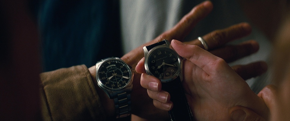 A still from the film 'Interstellar' depicting two hands with analog watches. One hand is outstretched and the other hand is holding the watch.