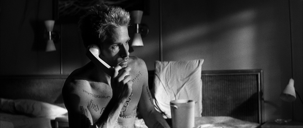A black and white still from the film 'Memento' depicting a man covered in tattoos